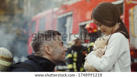 Portrait of rescued little asian girl with firefighter man standing near fire truck. Firefighter in fire fighting operation