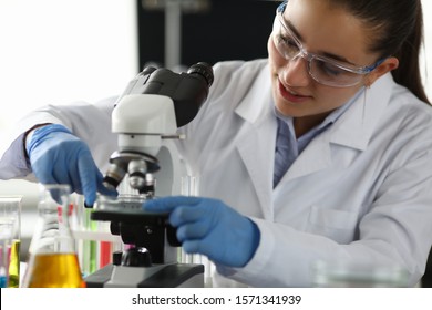 Portrait of research technician putting some substance under microscope in laboratory office. Smiling woman in protective uniform. Science and investigation concept