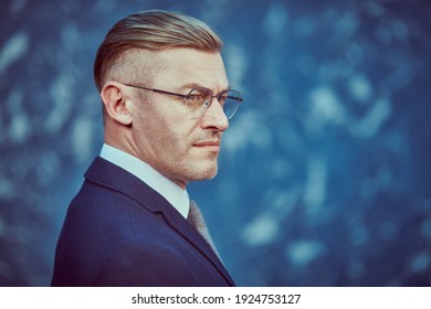 Portrait of a respectable mature man in a suit and glasses on a blue background. Businessman portrait. Copy space.