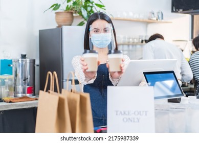 Portrait Of Restaurant Waiter Wear Mask  Holding Cup Of Coffee In Cafe. Attractive Beautiful Woman Worker In Apron Work In Coffeehouse And Hold Beverages Cups With Two Hands Due To Covid-19 Pandemic.