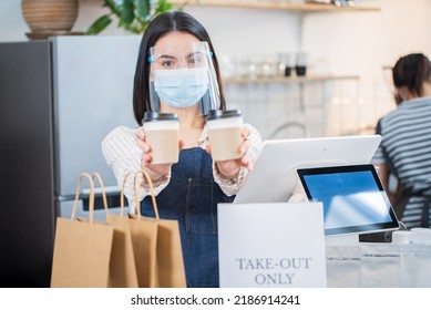 Portrait Of Restaurant Waiter Wear Mask Handing Cup Of Coffee In Cafe. Happy Attractive Beautiful Woman Worker Work In Coffeehouse And Holding Beverages Cups With Two Hands Due To Covid-19 Pandemic.