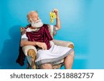 Portrait of rich ancient citizen politician sit throne hold grape empty space isolated on blue color background