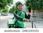 Portrait Rider food delivery man wearing green uniform and helmet cycling a bicycle the food service to customer. Happy delivery man with green backpack shipping of goods to customers.