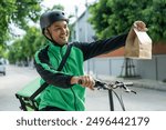 Portrait Rider food delivery man wearing green uniform and helmet cycling a bicycle the food service to customer. Happy delivery man with green backpack shipping of goods to customers.