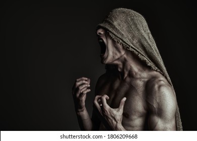 Portrait Of A Roaring Muscular Man With Burlap On His Face, Expressing Rage And Suffering. Studio Shot On A Black Background. Horrors And Halloween.