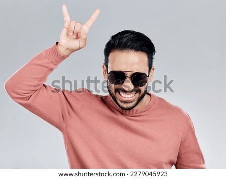 Portrait, rock on and hand gesture with a man in studio on a gray background feeling crazy or energetic. Face, rocker or hardcore and a male posing with a devil horns sign or symbol at a concert
