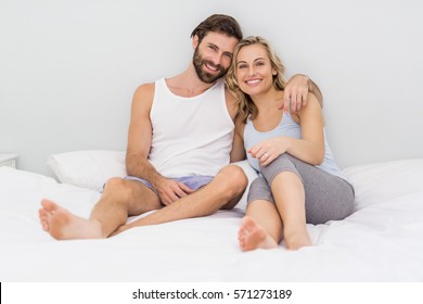 Portrait Of Romantic Couple Sitting On Bed In Bedroom