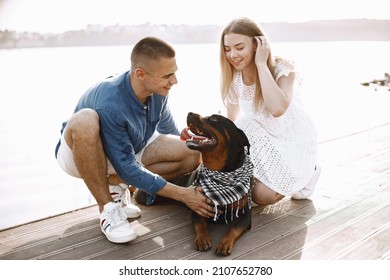 Portrait Of A Romantic Couple With Their Rotweiller Near The Lak