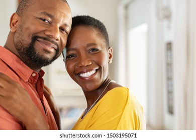 Portrait Of Romantic Mature Couple Embracing And Looking At Camera. Smiling Black Man And Woman Together In New Home. Closeup Face Of Satisfied Happy Couple In Their New Apartment With Copy Space.