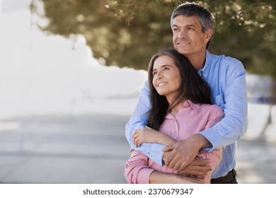 Portrait Of Romantic Mature Couple Embracing Outdoors And Looking Away, Loving Middle Aged Man And Woman Hugging And Smiling, Beautiful Spouses Enjoying Date Outside, Having Walk In City, Copy Space - Powered by Shutterstock