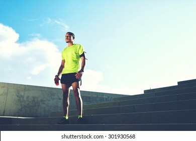 Portrait of a runner man with armband on the arm rest after jogging while standing on ladder against the sky background with copy space area for your text message information,sportsman taking a break 
