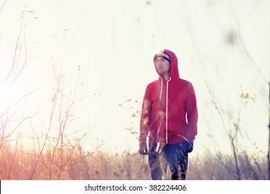 Portrait of runner in red jacket, black pants and gloves in the field with headlamp. Trail running, jogging. Cold autumn winter windy weather, yellow grass, morning sun. - Powered by Shutterstock