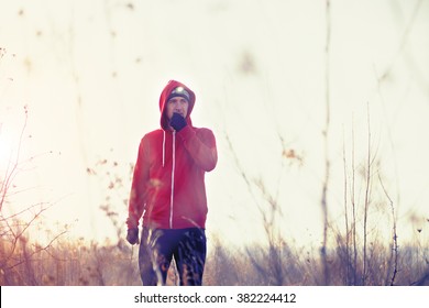 Portrait of runner in red jacket, black pants and gloves with headlamp standing in the field and rest after morning run. Trail running, jogging. Cold autumn winter windy weather, yellow grass. - Powered by Shutterstock