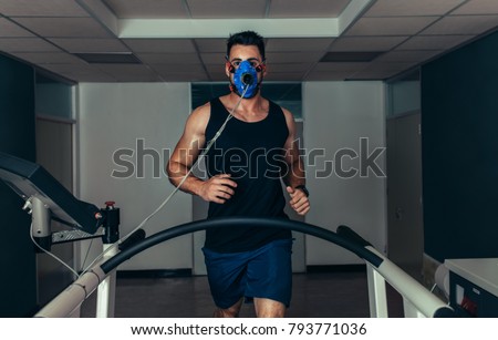 Portrait of runner wearing mask on treadmill in sports science laboratory. Sports man running on treadmill and monitoring his fitness performance.