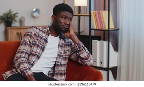 Portrait Of Sad Of African American Man Sitting At Home Looks Pensive Thinks Over Life Concerns Or Unrequited Love, Suffers From Unfair Situation. Problem, Break Up, Depressed Feeling Bad Annoyed