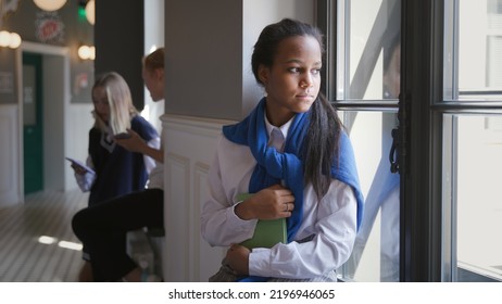 Portrait of sad African-American teen student sitting on window sill in corridor. Upset schoolgirl having problems with education or failing examination looking out of window