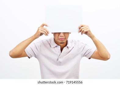 Portrait Of Sad Asian Man Hand Holding White Blank Paper Card Covering His Eyes, Standing Isolated On Plain Background.