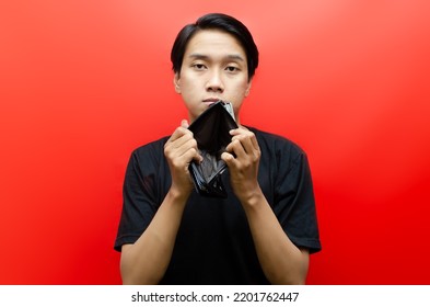 Portrait Of Sad Asian Man Showing  His Empty Wallet And Looking At Camera Isolated Over Red Background. Bankrupt Concept. Jobless Concept.