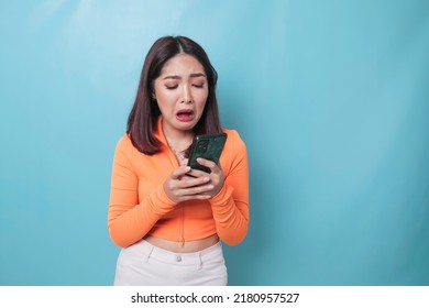 A Portrait Of A Sad Asian Woman Looking At Her Smartphone Over Blue Background