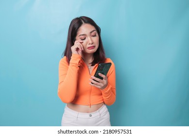 A Portrait Of A Sad Asian Woman Looking At Her Smartphone Over Blue Background