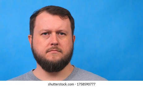 Portrait Of A Sad Bearded Man In A Gray T-shirt Singing And Talking To The Camera On A Blue Background. High Quality 4k Footage