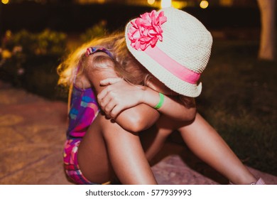 Portrait of sad blond little girl sitting on the ground.