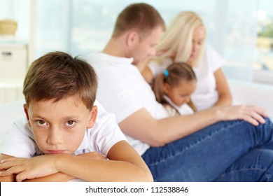 Portrait Of Sad Boy On Background Of His Parents And Sister