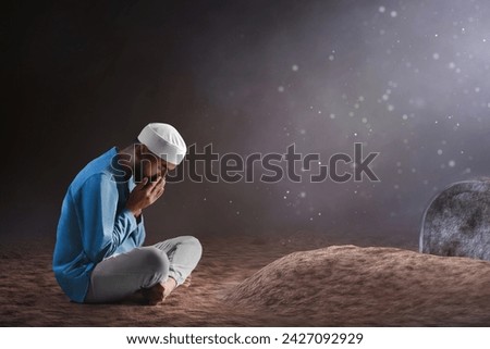 Portrait of sad crying young asian muslim man with beard praying on graveyard cemetery