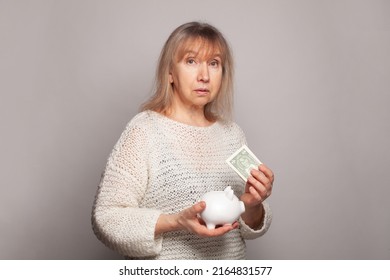 Portrait Of Sad Frustrated Senior Woman Holding A Piggy Bank And Us Dollar Money Banknotes.