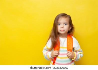 Portrait Of A Sad Girl With A Backpack. European Appearance. Emotions. Back To School. The Child Does Not Want To Go To School. Learning Difficulties. Academic Year. Yellow Background, Space For Text.