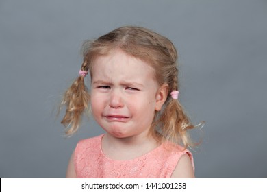 Portrait of sad girl and pink dress, studio, child crying on gray background