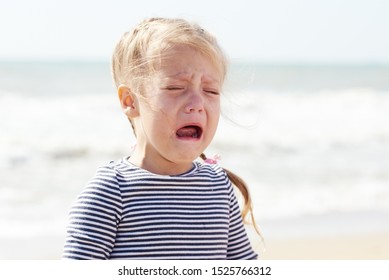 Portrait Of Sad Little Child Girl Crying, On Summer Beach Background. The Child Is Lost And Looking For Parents