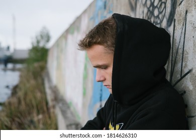 portrait of a sad lonely teenager / young guy in a black hoodie in an abandoned place near the port