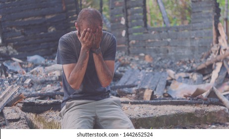 Portrait of a sad man on the background of a burned house, after fire . Consequences of fire disaster accident. Ruins after fire disaster, despair concept.