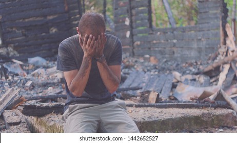 Portrait of a sad man on the background of a burned house, after fire . Consequences of fire disaster accident. Ruins after fire disaster, despair concept.