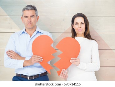 Portrait Of Sad Mature Couple Holding Broken Hearts Against Wooden Background