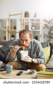 Portrait Of Sad Middle-aged Man Eating Takeout Noodles While Watching TV At Home In Bachelors Pad, Copy Space