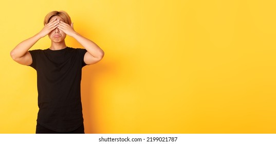 Portrait Of Sad And Miserable Asian Guy Shut Eyes And Sulking Upset, Standing Yellow Background