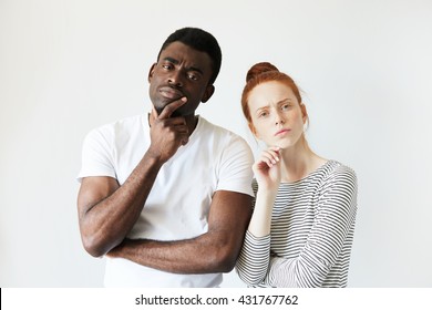 Portrait Of Sad Mixed-race Couple. Beautiful Caucasian Woman With Red Hair And Handsome African Man, Looking At The Camera With Unhappy Offended Expression, Not Speaking To Each Other. Body Language