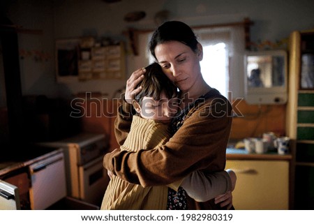 Portrait of sad poor mature mother hugging small daughter indoors at home, poverty concept.