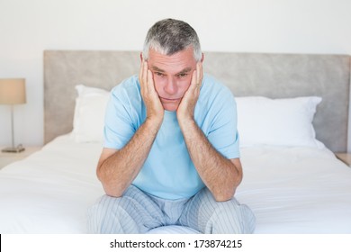 Portrait Of Sad Senior Man With Head In Hands Sitting On Bed At Home