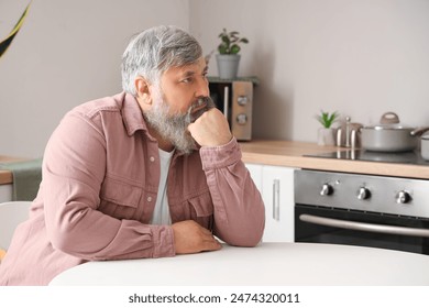 Portrait of sad senior man sitting at table in kitchen - Powered by Shutterstock