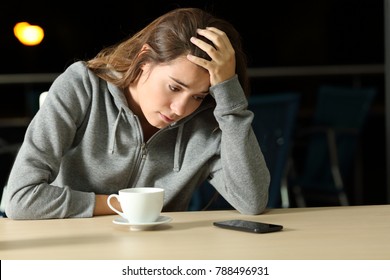 Portrait Of A Sad Teen Waiting For A Smart Phone Message Sitting In A Bar In Tha Night