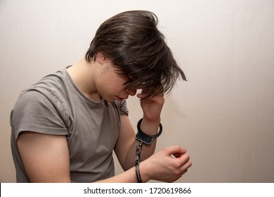 Portrait Of A Sad Teenager In Handcuffs On A Gray Background, Medium Plan. Juvenile Delinquent, Criminal Liability Of Minors. Members Of Youth Criminal Groups And Gangs.