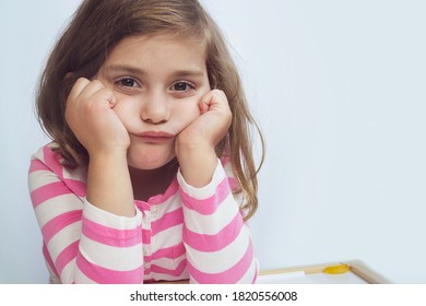 Portrait of a sad tired frustrated girl sitting at the table, girl being bored.  Learning difficulties, education concept