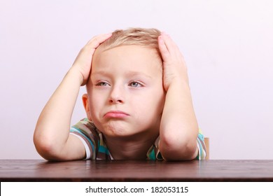 Portrait Of Sad Unhappy Tired Blond Boy. Child Kid Making Silly Funny Face At The Table Interior. Emotions.