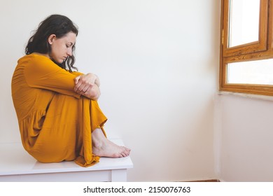 Portrait Of A Sad Woman In A Yellow Dress, Pensive Brunette, Sad Mood, Melancholy, Girl In A White Room Sits On A Table