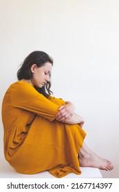 Portrait Of A Sad Woman In A Yellow Dress, Pensive Brunette, Sad Mood, Melancholy, Girl In A White Room Sits On A Table