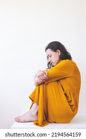 Portrait Of A Sad Woman In A Yellow Dress, Pensive Brunette, Sad Mood, Melancholy, Girl In A White Room Sits On A Table