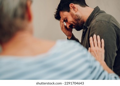 Portrait of a sad young man on group therapy meeting discussing addiction and mental health problems. Multiracial people talking about their mental health issues. Senior woman comforting him.